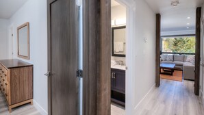 A modern interior with a wooden cabinet, a dark wooden door, a bathroom with a mirror, and a seating area with a sofa and a table. - Newly remodeled condo just steps from the gondola, hot tub, sleeps 4! (Vail)