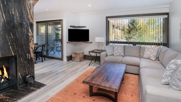 A modern living room with a fireplace, a sofa, a coffee table, and a TV mounted on the wall. - Newly remodeled condo just steps from the gondola, hot tub, sleeps 4! (Vail)
