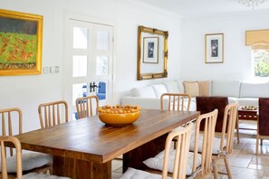 Ein Essbereich mit Holztisch, Stühlen, einer Fruchtschale und einem weißen Sofa im Hintergrund.