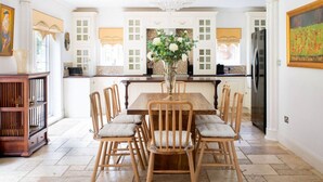 Een eetruimte met een houten tafel, zes stoelen, een vaas met bloemen en een keuken op de achtergrond.