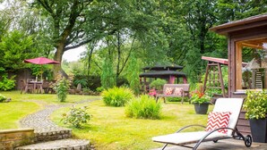 Een tuin met een prieel, een houten terras, een stoel en een tafel.