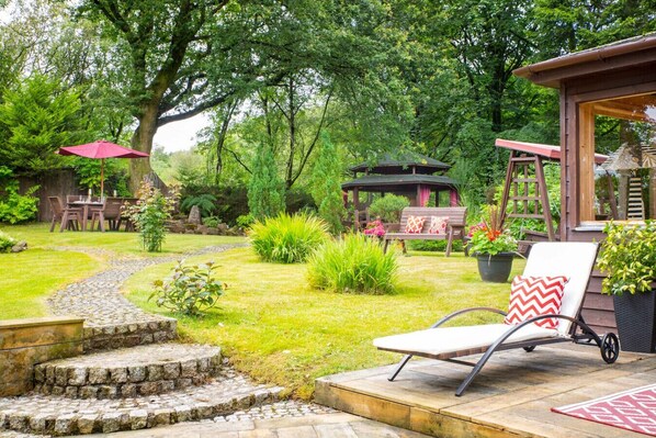 Ein Garten mit einem Gazebo, einer Holzterrasse, einem Stuhl und einem Tisch.