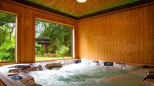 Een houten spa-ruimte met een whirlpool, grote ramen en uitzicht op een tuin.