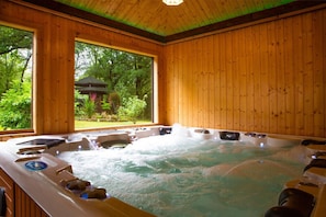 Ein Spa-Raum aus Holz mit Whirlpool, großen Fenstern und Blick auf einen Garten.