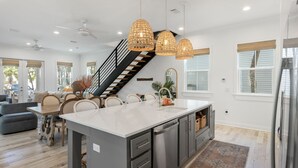 Cozinha espaçosa com uma ilha grande, luminárias pendentes modernas e uma escada que leva a um andar superior.