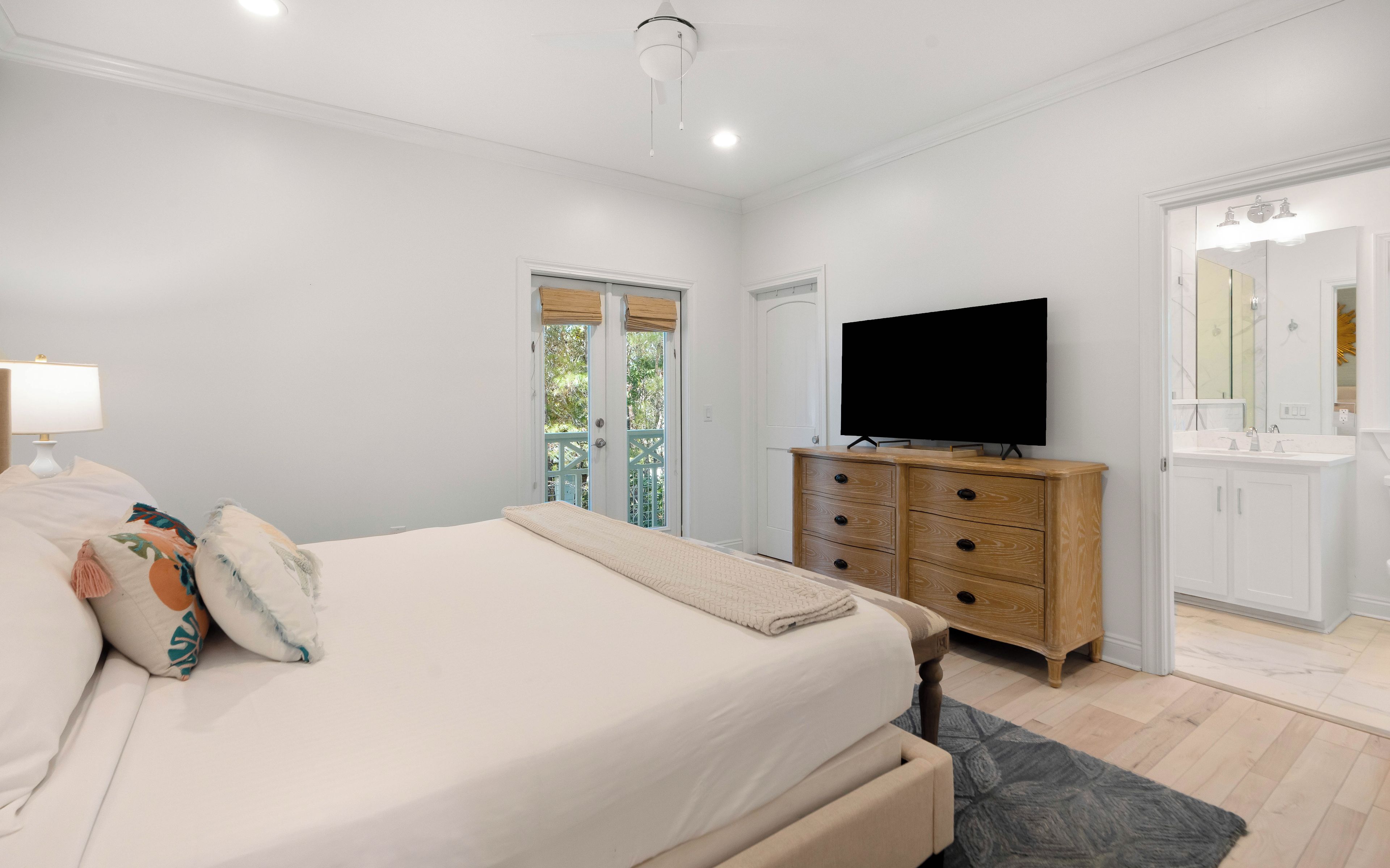 A bedroom with a bed, a dresser, a television, and a bathroom visible through an open door.