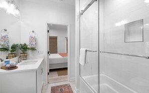 A modern bathroom with a shower, a sink, and a small bed.