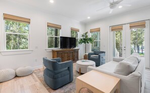 Un salón amplio con televisor de pantalla plana, asientos cómodos y ventanas grandes con persianas.