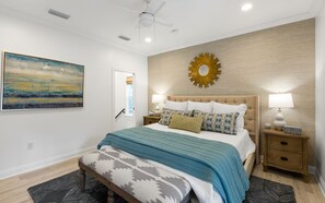 A bedroom with a bed, bedside tables, a ceiling fan, a wall-mounted mirror, and a painting.