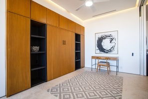 A room with a wooden wardrobe, a desk with a chair, a patterned rug, and a ceiling fan. - Soho PV • 2 Workspaces, Pool, Gym & Rooftop Bar (Puerto Vallarta)