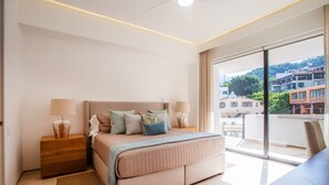 Une chambre à coucher moderne avec un grand lit, des lampes de chevet, une table de chevet en bois et une vue sur les immeubles par une grande fenêtre.