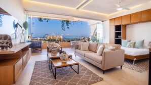 Un salon moderne avec un canapé, une table basse et des fauteuils, un lit et une vue sur l’océan.