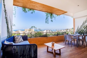 A balcony with a view of the city, a sofa, a table, and chairs. - Soho PV • 2 Workspaces, Pool, Gym & Rooftop Bar (Puerto Vallarta)