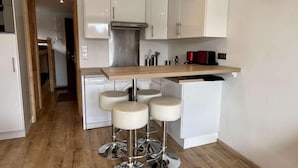 Una cocina moderna con armarios blancos, extractor de acero inoxidable y encimera de madera. Hay tres taburetes de bar blancos con patas de metal.