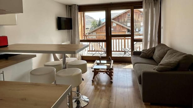 Una sala de estar moderna con una mesa de comedor de madera, sillas blancas, un sofá y un televisor montado en la pared.