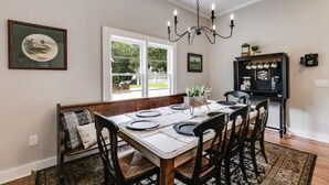A dining area with a wooden table set for four, a bench with cushions, a chandelier, and a window with a view of greenery.