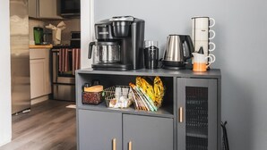 A kitchen area with a grey cabinet containing a coffee maker, a kettle, and a mug. - Cozy home, close to dining, entertaining, military bases, beaches and more. (North Charleston)