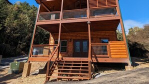 A two-story log cabin with a balcony on the upper floor, a front porch with steps, and a small front window. - Ern806 - Splashin' Views 2 Bedroom Cabin by RedAwning (Sevierville)
