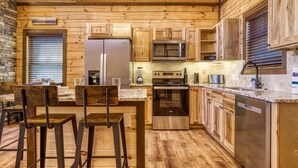 A modern kitchen with wooden cabinetry, stainless steel appliances, and a bar area with stools. - Ern806 - Splashin' Views 2 Bedroom Cabin by RedAwning (Sevierville)