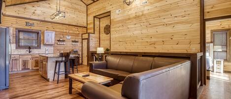 Een gezellig cabin interieur met houten plafond, een bank, een eethoek en een keuken.