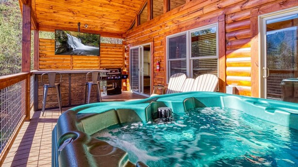 A wooden cabin with a hot tub, outdoor seating, and a waterfall view. - Ern806 - Splashin' Views 2 Bedroom Cabin by RedAwning (Sevierville)