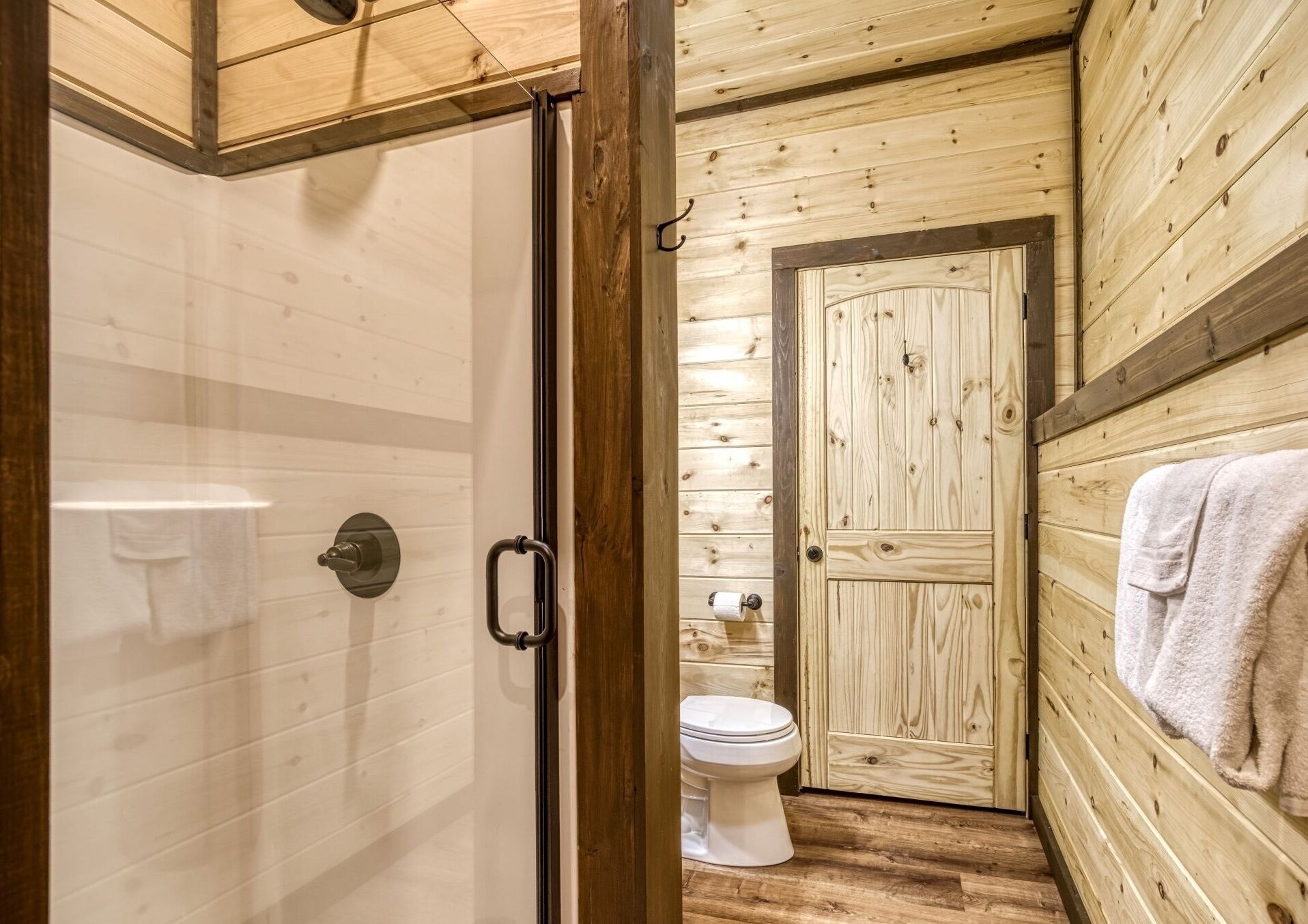 Un intérieur en bois comprenant une douche, des toilettes et une porte donnant sur une autre pièce.