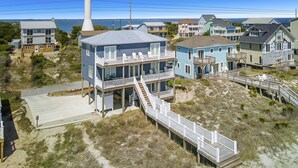 Une maison située sur la côte, dotée d’une terrasse à plusieurs niveaux et avec un phare en arrière-plan.