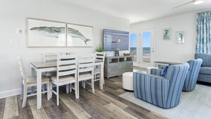 Un salon moderne avec un coin repas, comprenant une table à manger en bois, des chaises blanches et un canapé bleu à motifs.