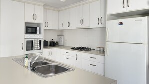 Eine moderne Küche mit weißen Schränken, einer Edelstahl-Spüle, einer Mikrowelle, einem Backofen, einem Gasherd und einem Kühlschrank.