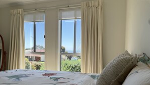 Ein Schlafzimmer mit Bett, Vorhängen und Blick auf Grünflächen und ein Gebäude.
