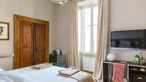 Ett hotellrum med en säng, ett skrivbord med en tv, ett element och ett fönster med gardiner.