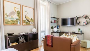 Ett modernt vardagsrum med en soffa, ett matbord för två personer, en platt-TV och en bokhylla.