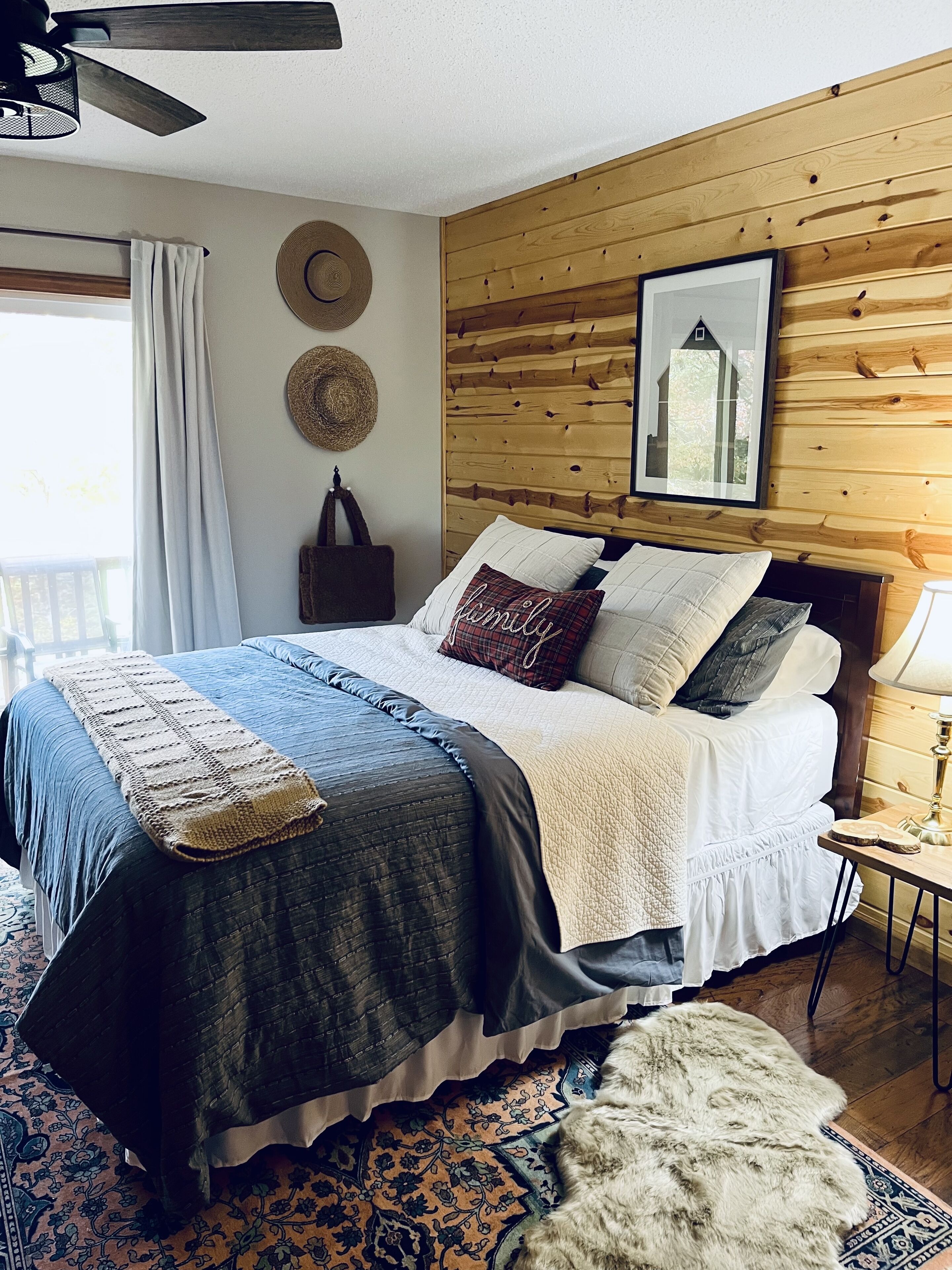 Un dormitorio con cabecera de madera, una cama grande con varias almohadas, una cesta tejida y una alfombra estampada.