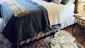 A bedroom with a wooden headboard, a large bed with multiple pillows, a woven basket, and a patterned rug.