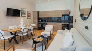 A modern living room with a sofa, dining table, and chairs, a kitchen with appliances, and a flat-screen TV on the wall. - Spacious Air-conditioned Apartment Center of Paris (Paris)