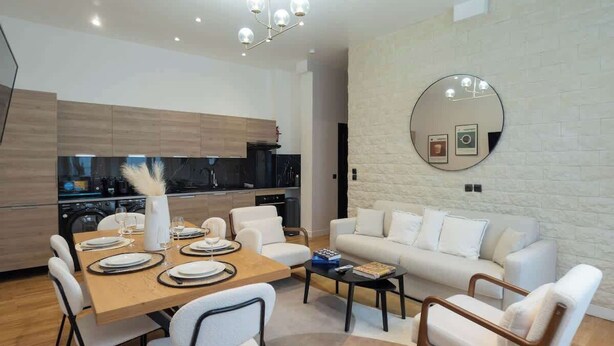 A modern living room with a dining area, white furniture, a round mirror, and a kitchen in the background. - Spacious Air-conditioned Apartment Center of Paris (Paris)