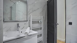A modern bathroom with a white marble sink, a glass shower enclosure, and a white towel rack. - Spacious Air-conditioned Apartment Center of Paris (Paris)