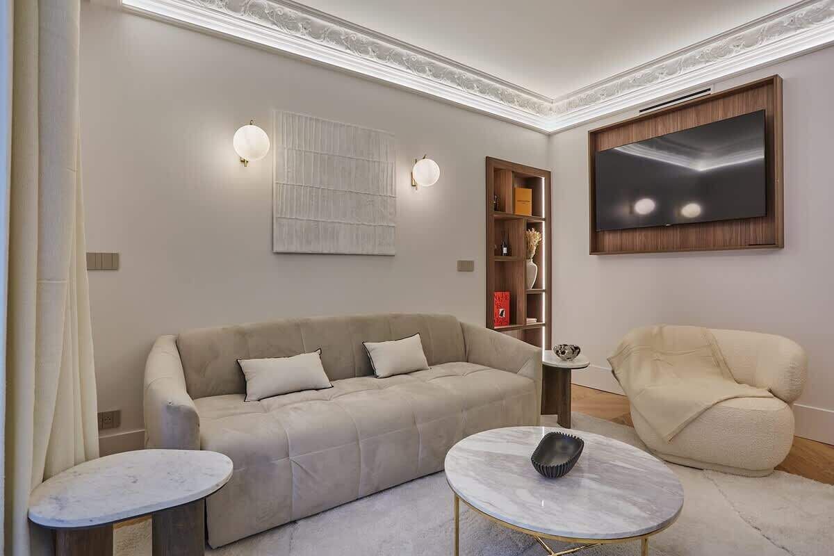 A modern living room with a beige sofa, two round tables, a flat-screen TV, and decorative wall art.