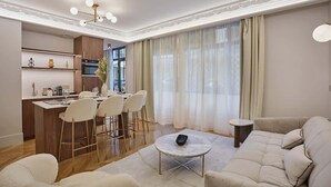 A modern living room with a sofa, a coffee table, and a dining area with chairs and a kitchen in the background.
