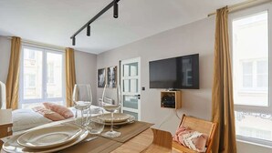 A modern hotel room with a dining area, a television mounted on the wall, and large windows with curtains. - Superb & New Studio Eiffel Tower (Paris)