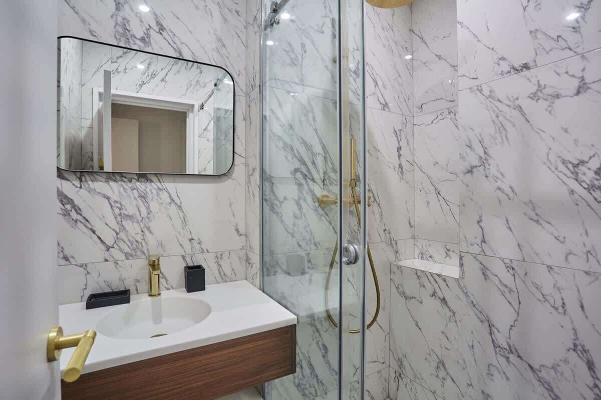A bathroom with a marble sink, a mirror, and a glass-enclosed shower.
