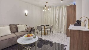 A modern living room with a sofa, a round coffee table, a dining area with a table and chairs, a chandelier, and a kitchen area with a sink and countertop. - Magnificent New Apartment Louvre Palais Royal (Paris)