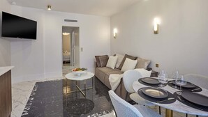 A modern living room with a flat-screen TV, a sofa, a dining table set for two, and a marble floor. - Magnificent New Apartment Louvre Palais Royal (Paris)
