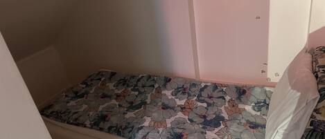 A small, single-bed room with a floral-patterned mattress and a white pillow.