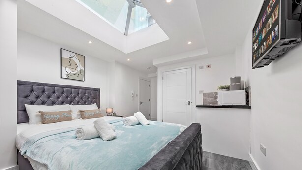 A modern bedroom with a large bed, a skylight, a flat-screen TV, and a small kitchenette. - Impeccable Ensuite Room in Finsbury Park Londonn19 (London)