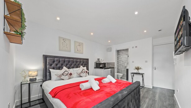 Un dormitorio moderno con una cama grande, una manta roja y un cabecero gris.