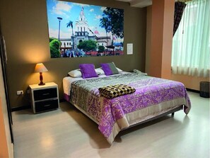 Relax in this serene space featuring a large bed, a nightstand with a lamp and drawer, and a beautiful framed picture above.