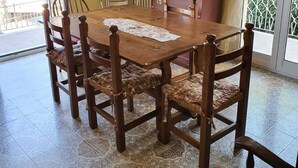Un coin repas avec une table et des chaises en bois, un téléviseur posé sur un meuble, et une fenêtre donnant sur un paysage verdoyant.