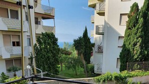 Un balcon doté d’une balustrade ornée, offrant une vue sur un quartier résidentiel avec des arbres et un bâtiment en arrière-plan.