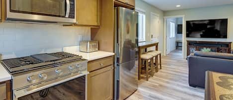 A modern kitchen with stainless steel appliances, wooden cabinets, and a wooden floor.